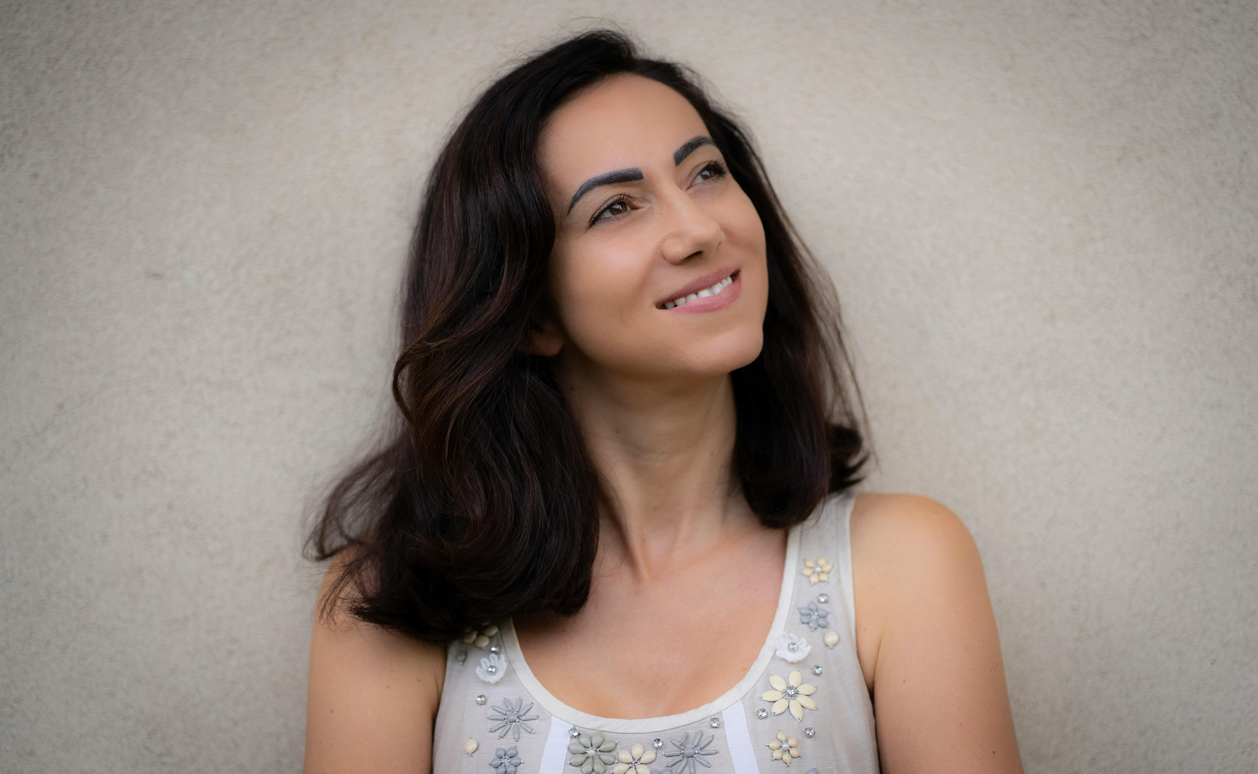 Portrait of a smiling woman in a floral top, leaning against a wall in Milan.