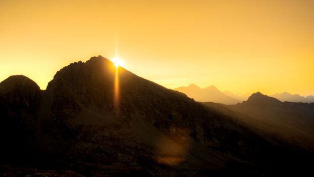 Dramatic sunrise over the peaks in Aosta Valley, Italy, casting warm tones.
