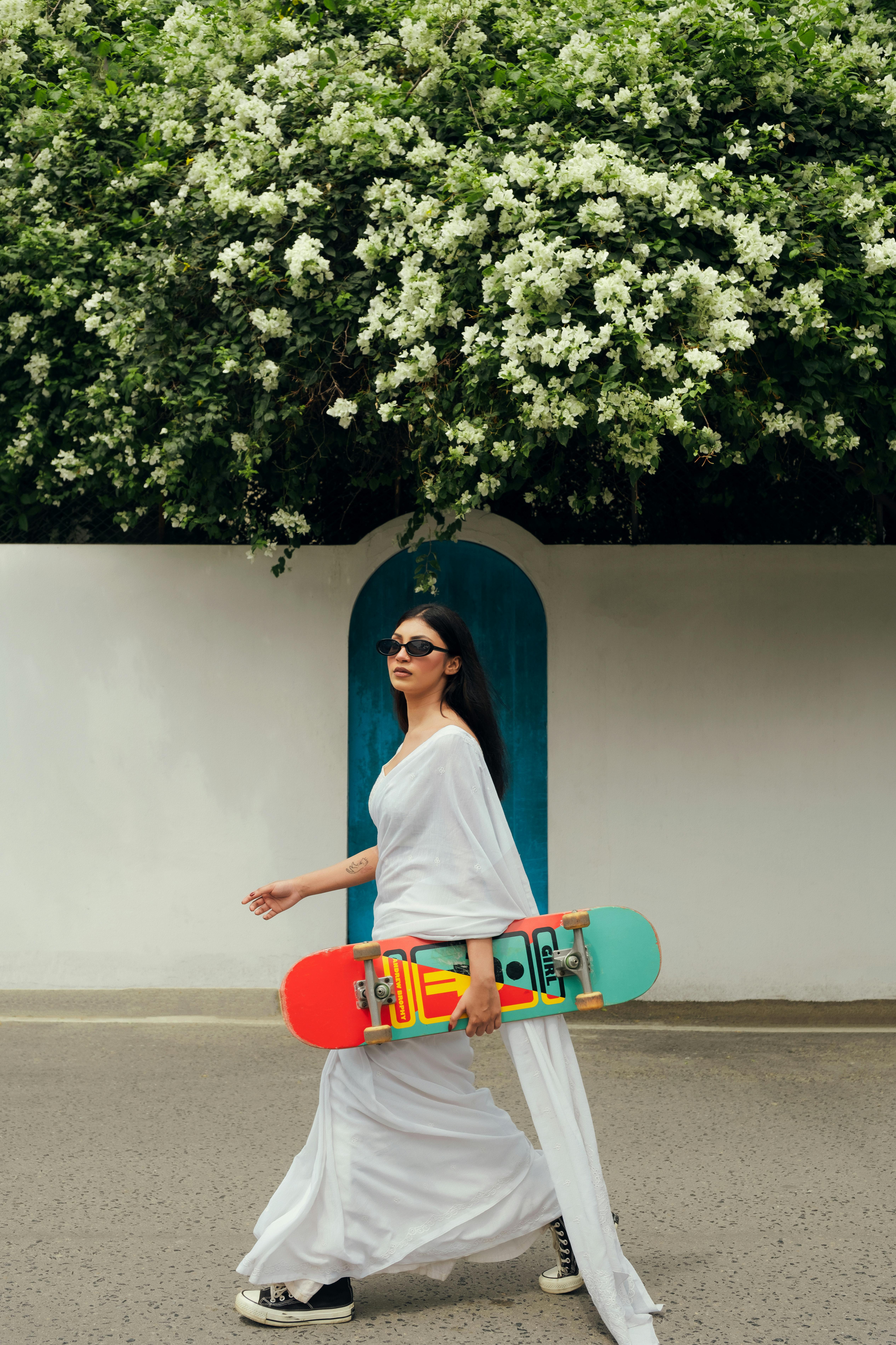 Stylish woman in white dress carrying a colorful skateboard, exuding casual elegance.