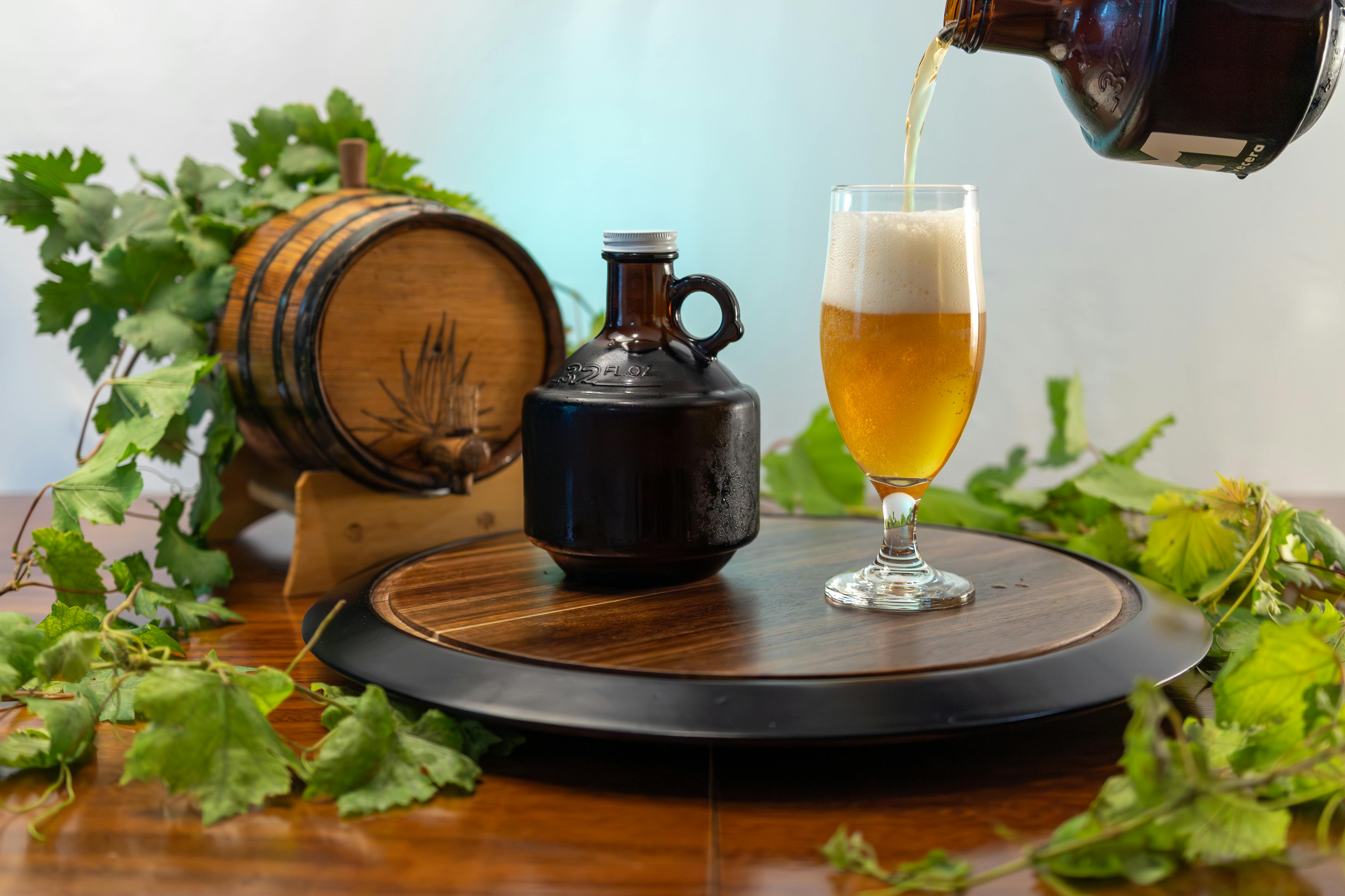 Craft beer being poured into a glass with a wooden barrel and vine leaves in the background for a rustic look.
