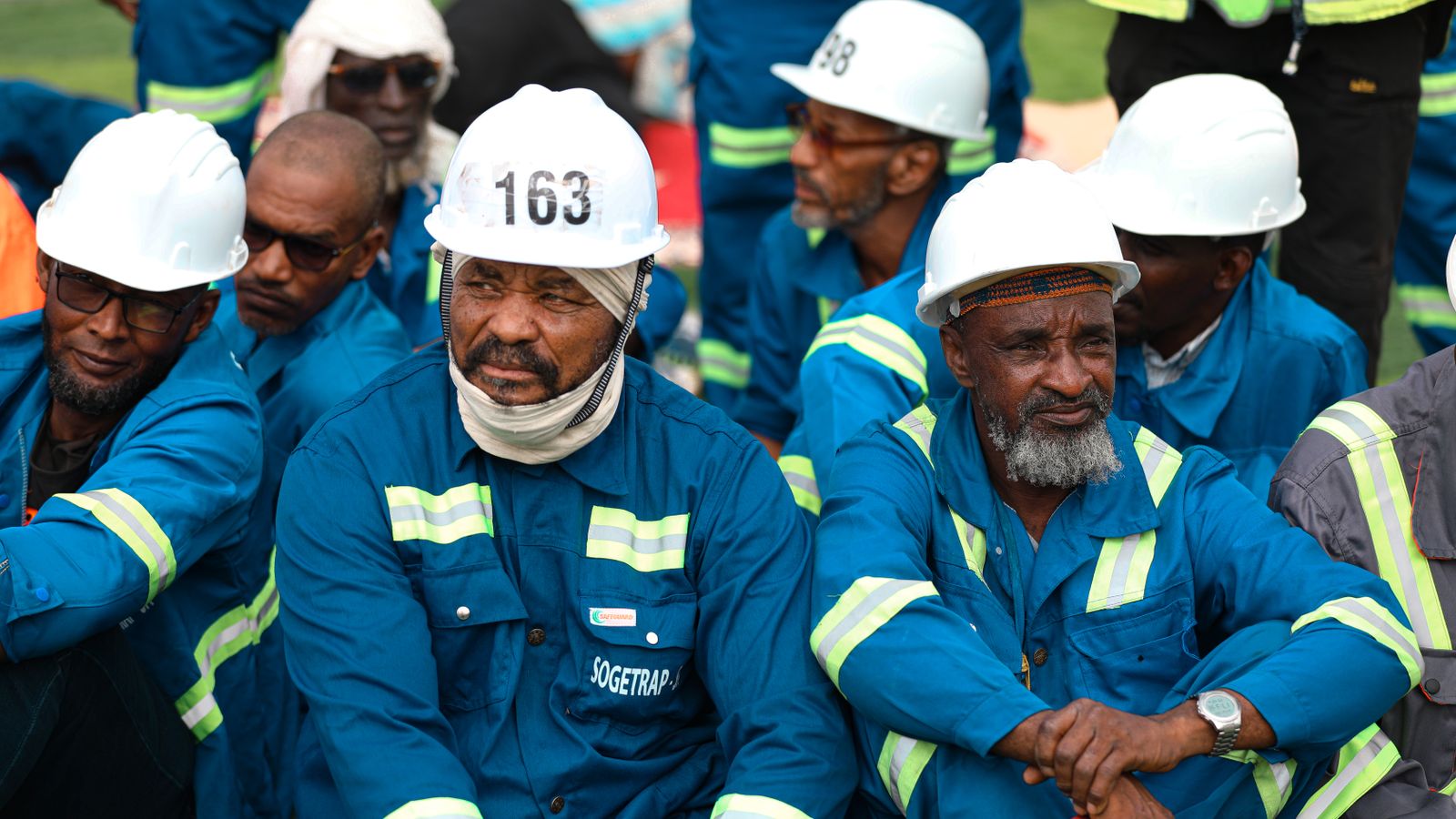 Construction workers in blue uniforms and white helmets during a break outdoors.