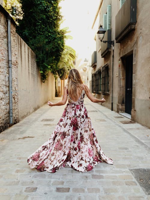 女人穿着白色和粉红色的花卉长裙站在巷子里