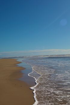 A clear sky and gentle waves create a peaceful beach scene with ample copyspace.