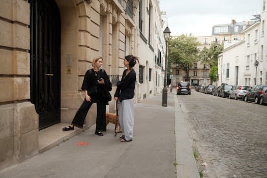 Two women with a dog converse outside a Parisian building on a cobblestone street.