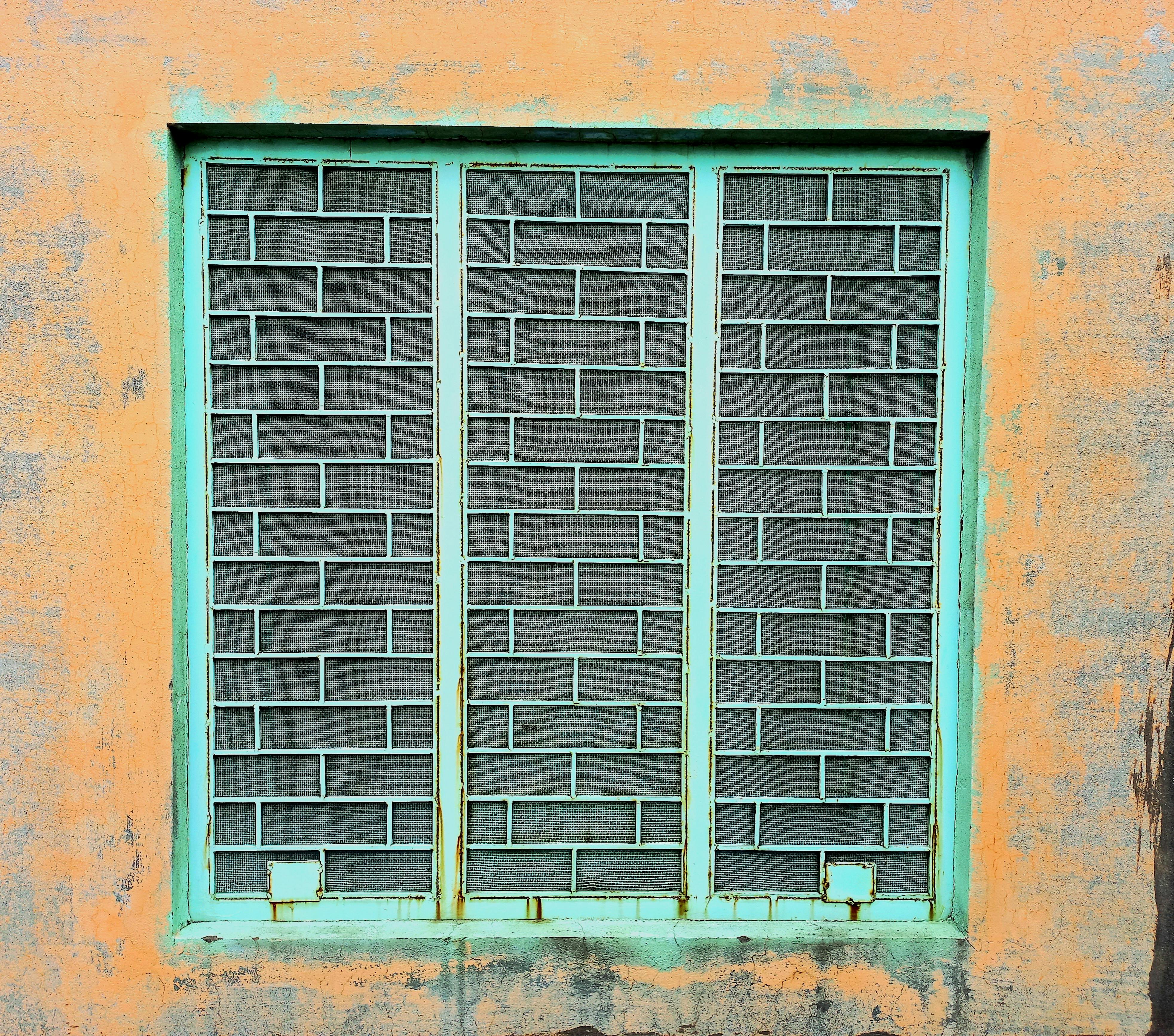 Zadarmo Rustikálne železné mrežové okno vsadené do textúrovanej, zvetranej steny, vyžarujúce vintage šarm. Fotka z fotobanky