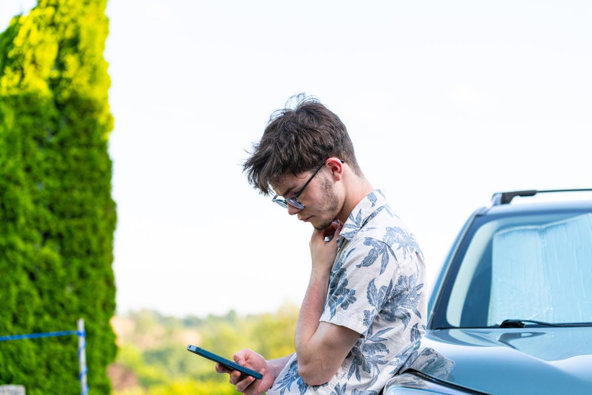Giovane uomo appoggiato a un'auto che usa lo smartphone all'aperto