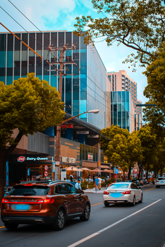 Urban street scene with modern buildings and vehicles, portraying a bustling city environment in daylight.