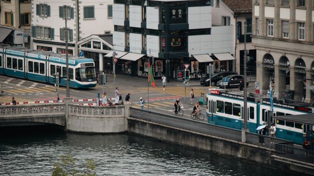 A bustling scene in Zürich featuring trams, cyclists, and pedestrians crossing a bridge.