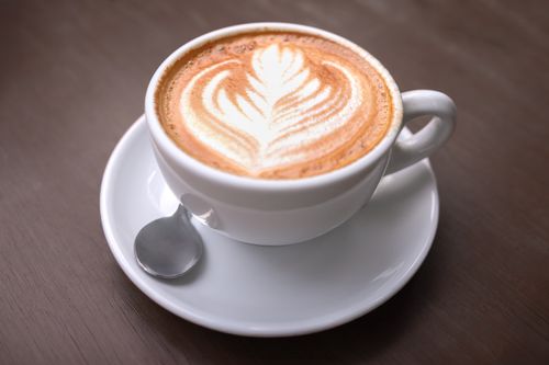 Free Close-up of a creamy latte with artistic leafy foam in a white cup on a wooden table, captured in Perú. Stock Photo