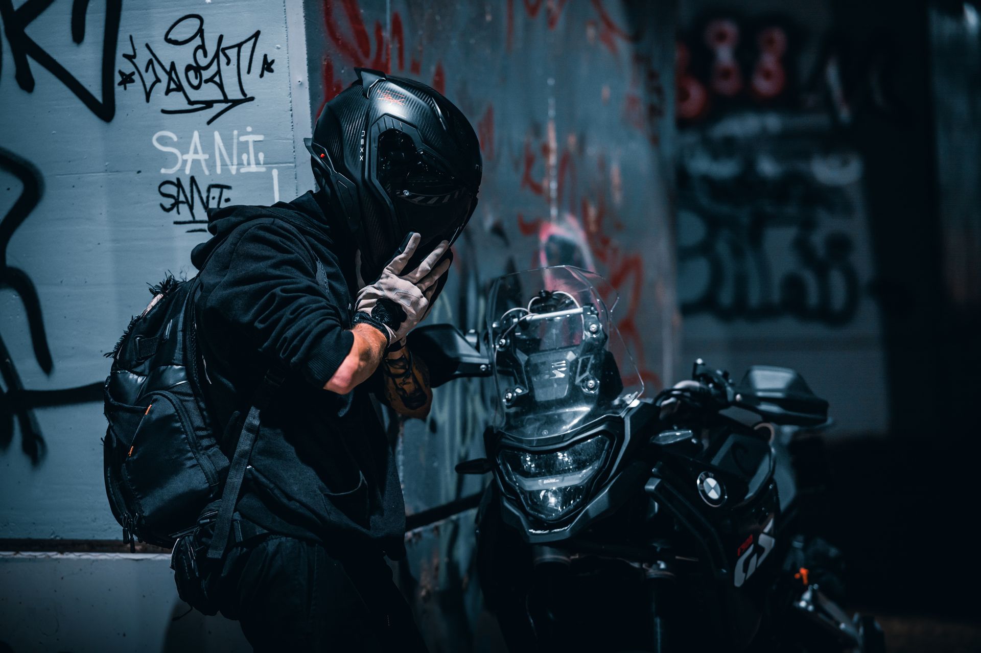 A motorcyclist poses in an urban alley setting with graffiti, creating a mysterious and edgy atmosphere.