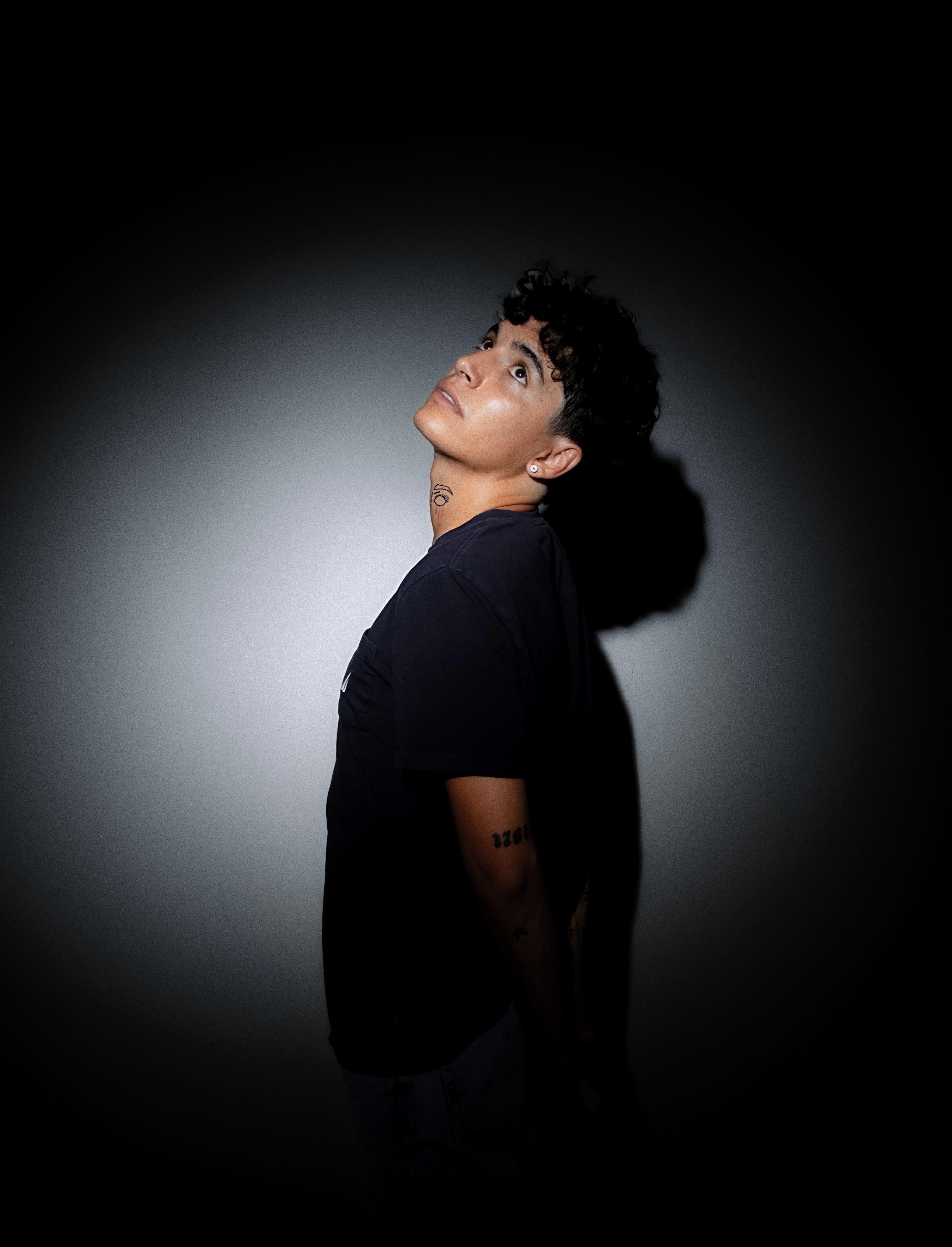 A moody portrait of a person looking up, illuminated by dramatic lighting in a dark setting.