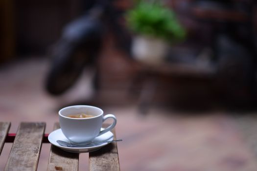 A warm cup of coffee sits on a wooden table outdoors, evoking a cozy and peaceful atmosphere.