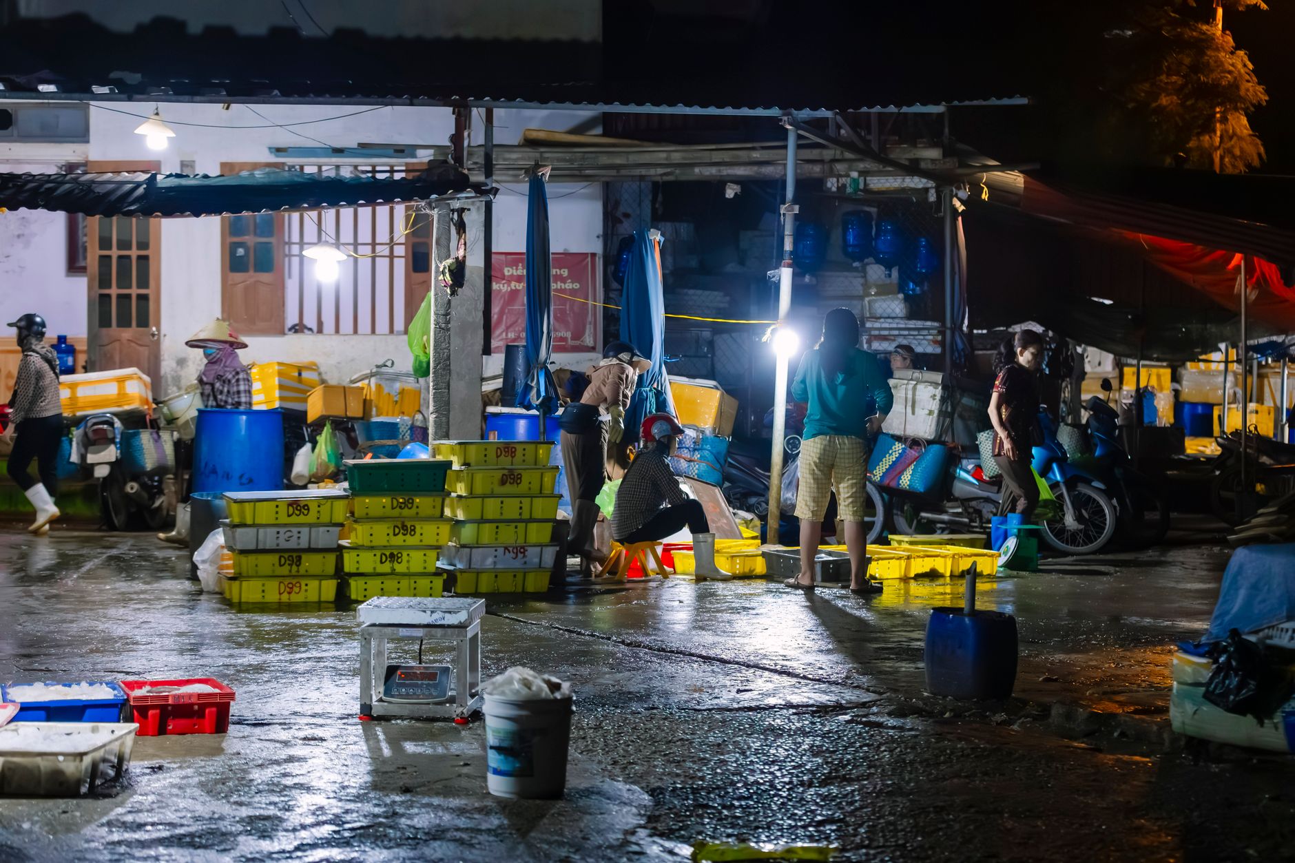 People working at an outdoor fish market at night, illuminated by artificial lights, showcasing a hectic atmosphere.