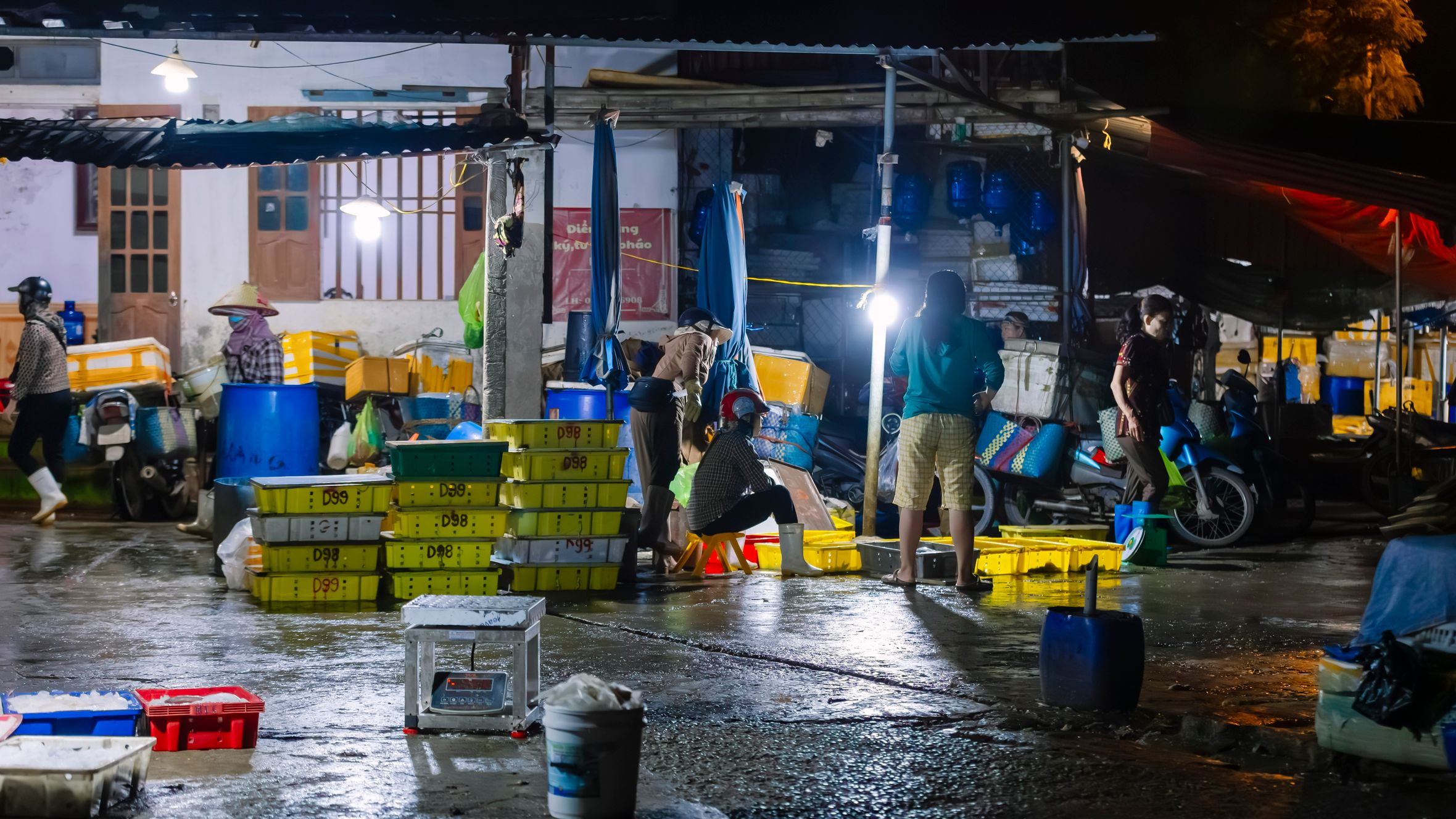 People working at an outdoor fish market at night, illuminated by artificial lights, showcasing a hectic atmosphere.