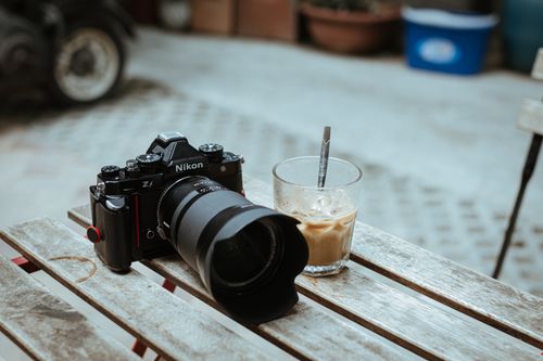 Free A camera and iced coffee placed on a rustic outdoor table, perfect for a photography-themed lifestyle shot. Stock Photo