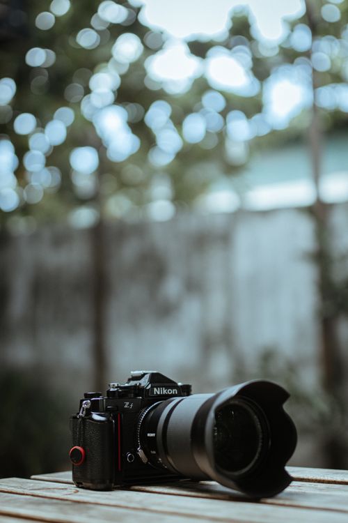 Free Nikon camera with lens placed on wooden surface outdoors with bokeh background. Stock Photo