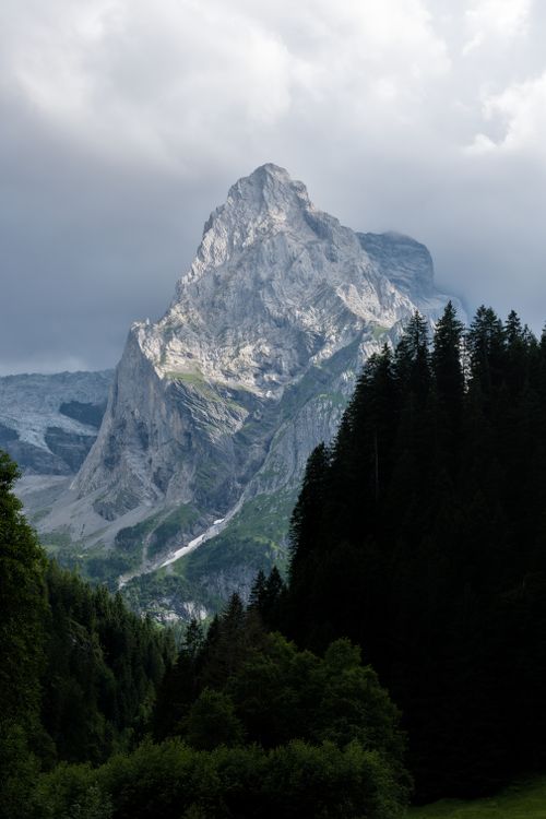 Free Dramatic alpine peak surrounded by dense forest and clouded skies, showcasing nature's grandeur. Stock Photo