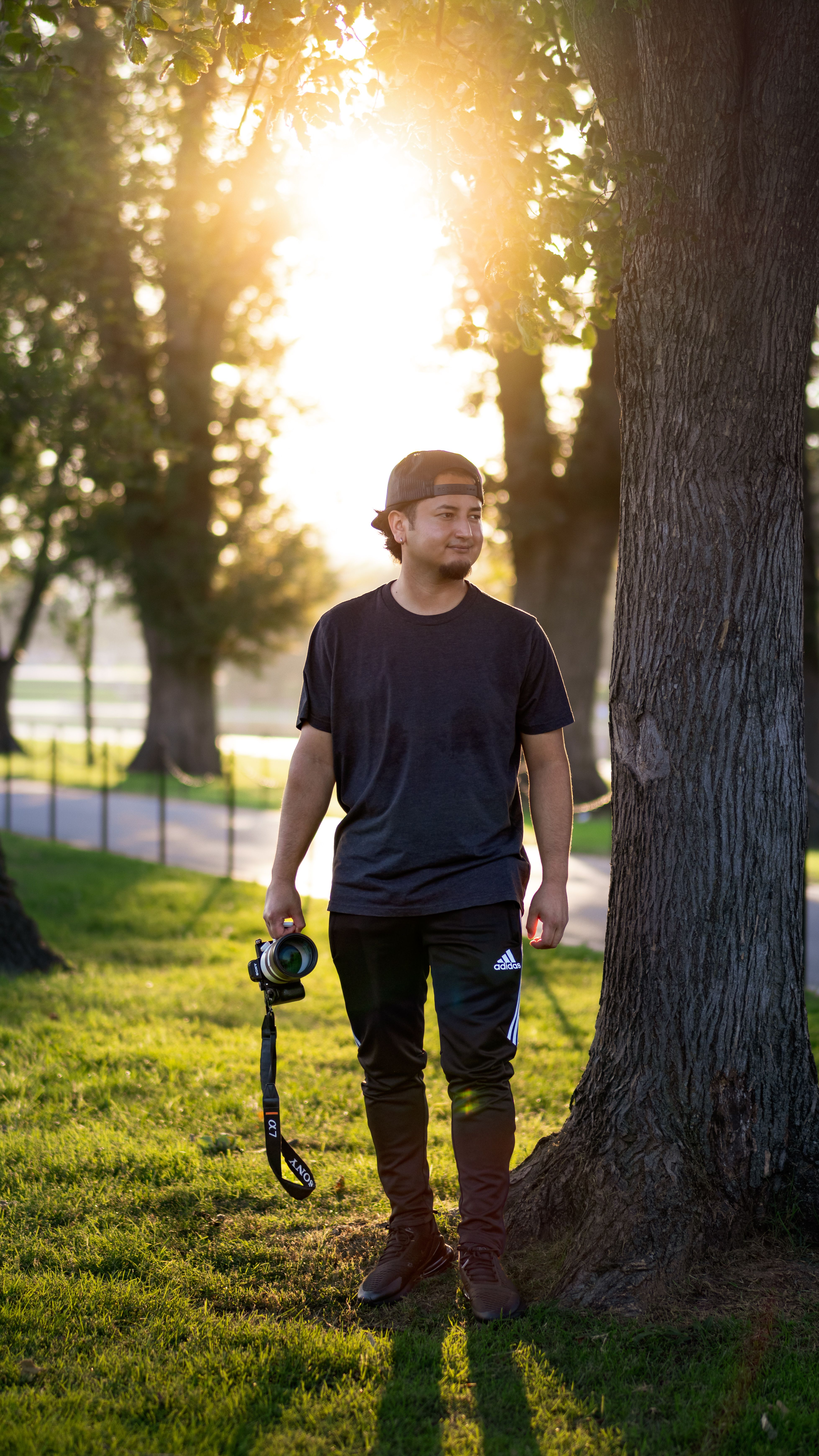 A young man stands outdoors in a Washington DC park during sunset, holding a camera.