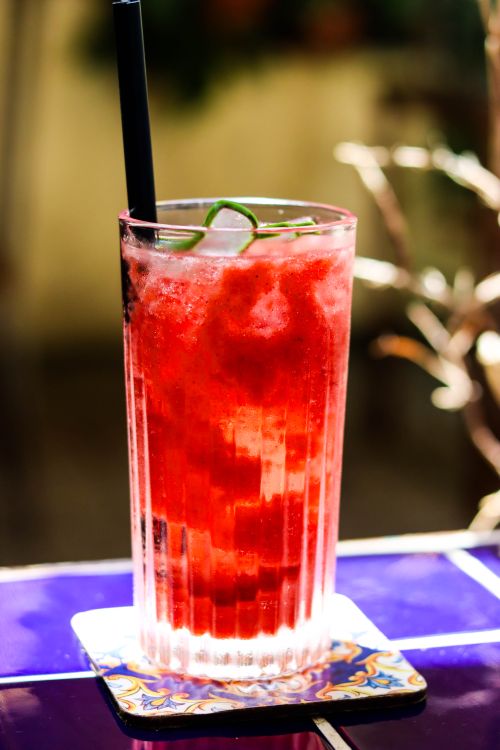 Free Delicious strawberry cocktail served in a tall glass with ice on a vibrant blue tile table. Stock Photo