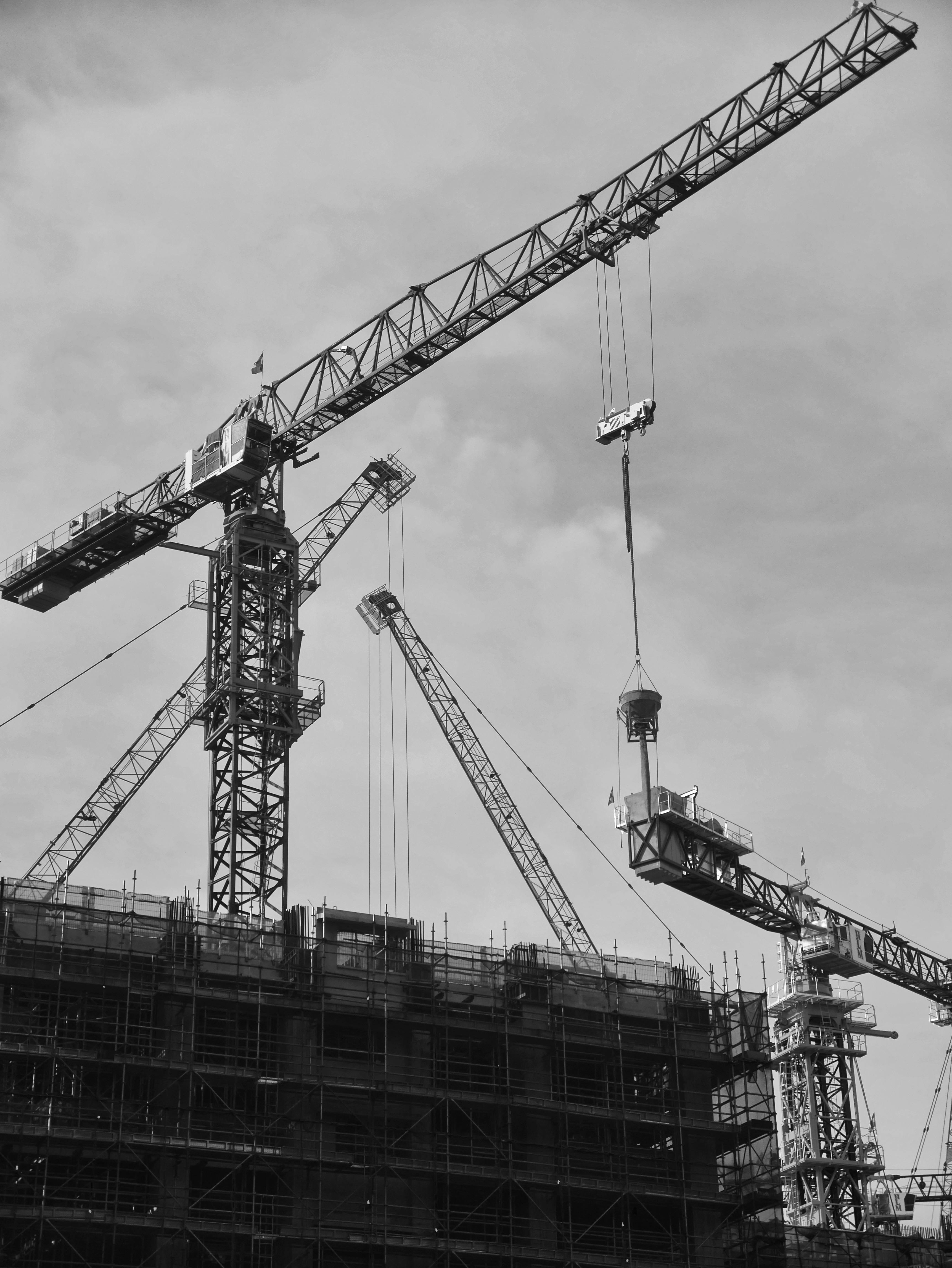 Grayscale Photo of a Tower Crane Under Cloudy Sky · Free