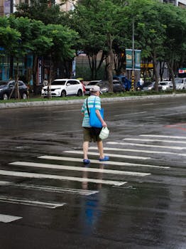 An elderly man crossing a rain-slicked street crosswalk in 新北市, Taiwan.