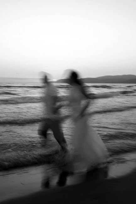 Blurred couple running on beach in black and white, capturing wedding joy.