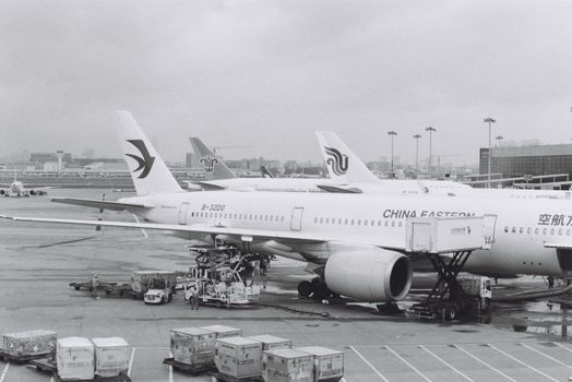 Black and white photograph of airplanes parked at an airport tarmac on a cloudy day.