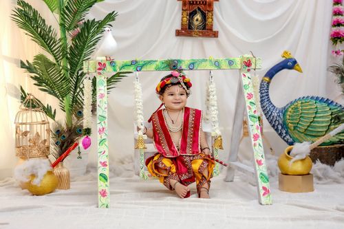 Free Happy child dressed as Krishna on a beautifully decorated swing indoors. Stock Photo