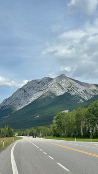 A winding highway leads to a majestic mountain under a bright summer sky, ideal for travel and nature enthusiasts.