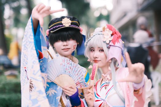 Cosplay enthusiasts in vibrant costumes posing outdoors with fans and peace signs.