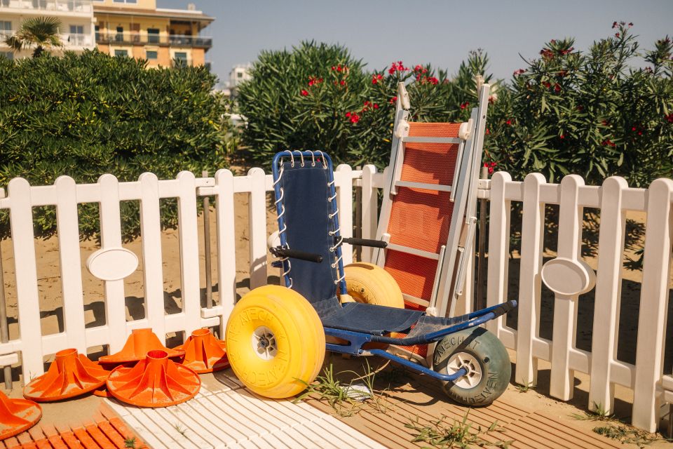 Sedia a rotelle da spiaggia accanto all'attrezzatura di salvataggio vicino a una recinzione bianca in una giornata di sole.
