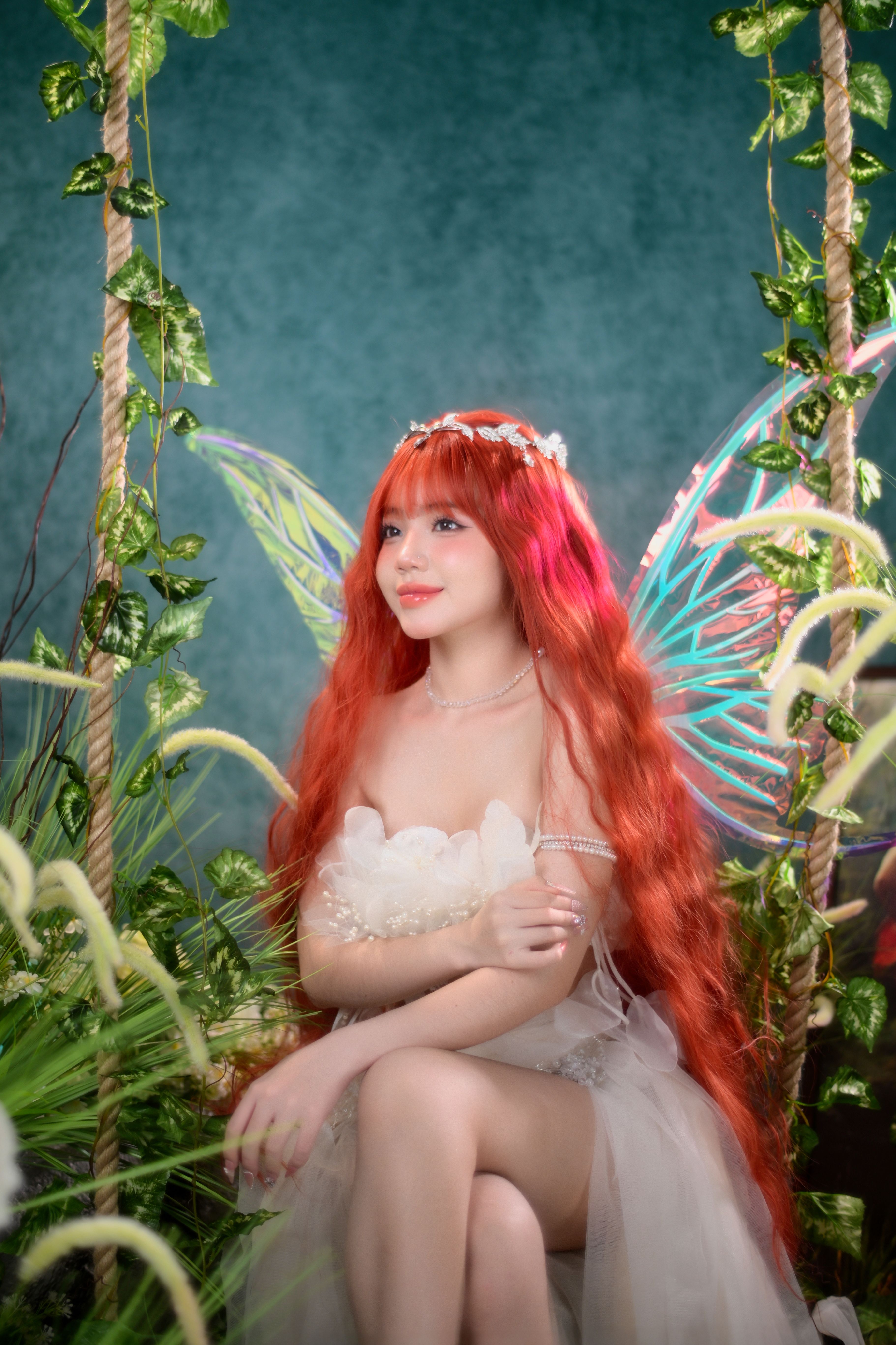 A beautiful woman with fairy wings and red hair amidst lush greenery indoors.