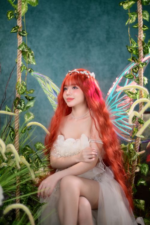 Free A beautiful woman with fairy wings and red hair amidst lush greenery indoors. Stock Photo