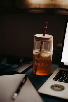 A warm, cozy workspace with a refreshing iced tea, laptop, and notepad, perfect for productivity.