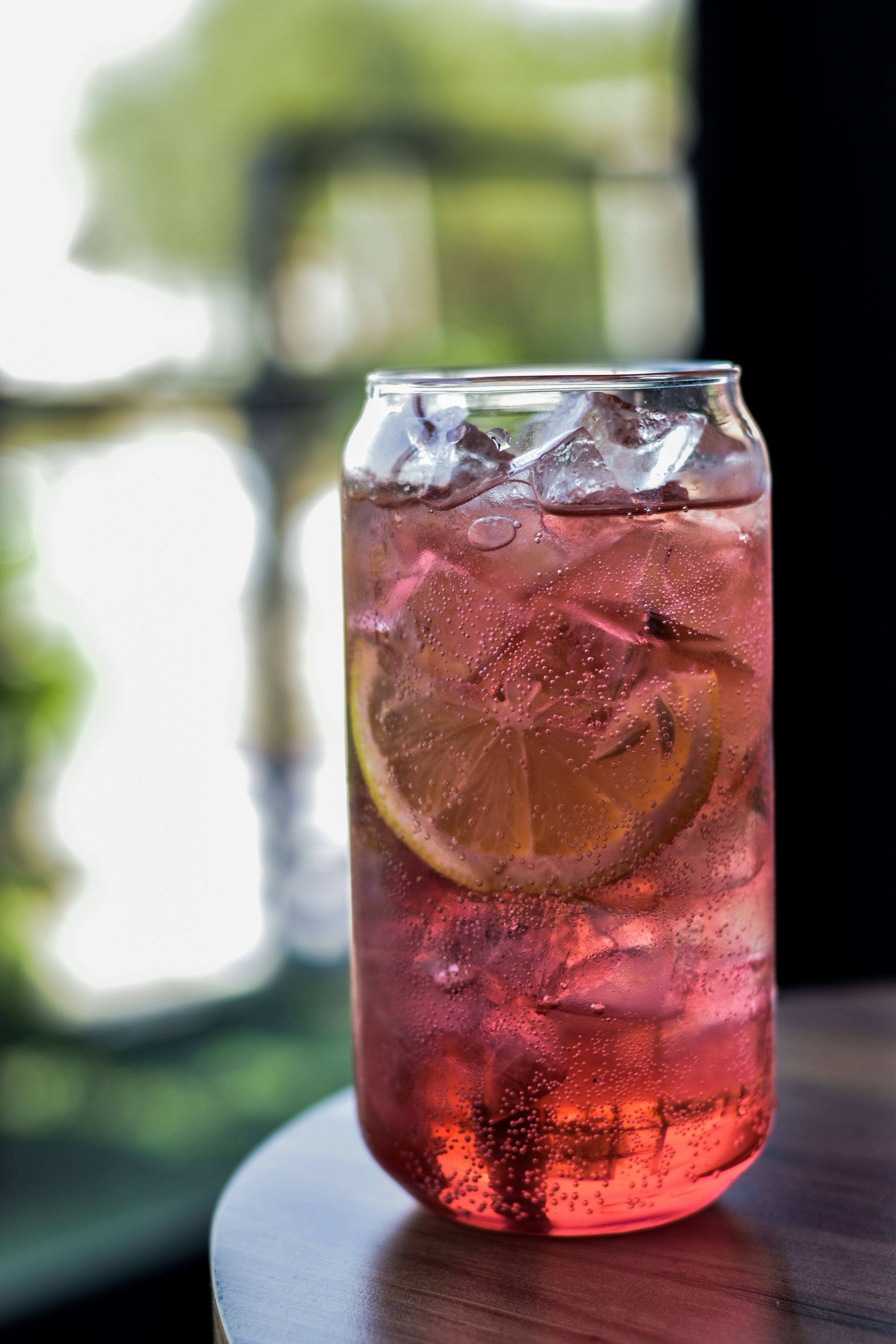 A tall glass of pink fizzy soda over ice with a slice of lemon
