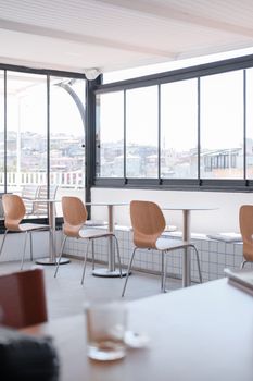 Sunlit cafe interior with empty tables and a panoramic city view.