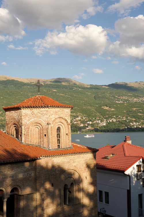 Free Scenic view of a historic church by Lake Ohrid, surrounded by mountains and bright sky. Stock Photo