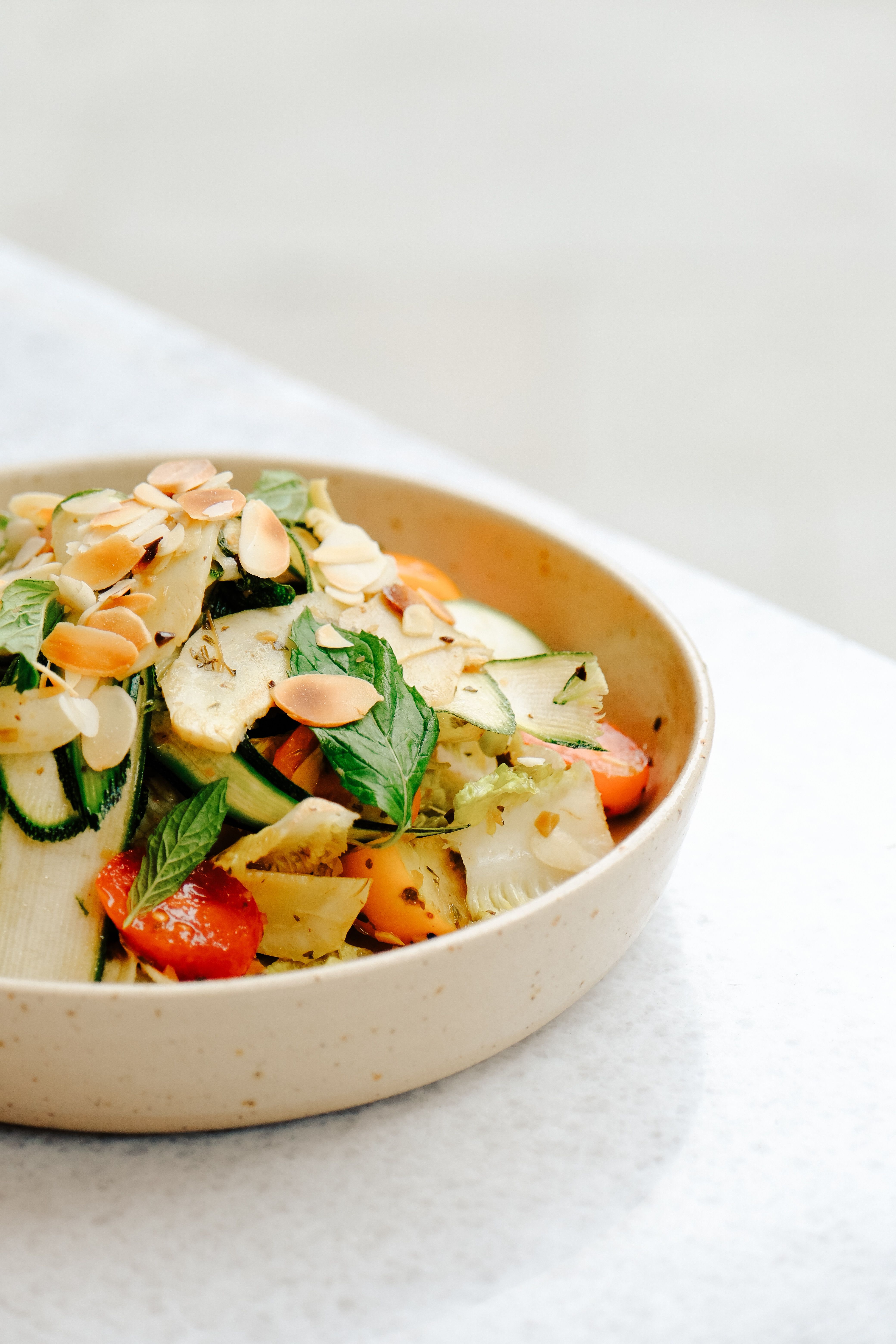 Colorful grilled vegetable salad topped with almonds served in a ceramic bowl.