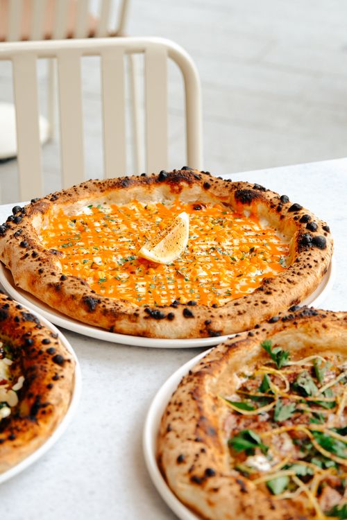 Free Close-up of artisan pizzas with bright toppings and lemon wedge on a white table. Stock Photo