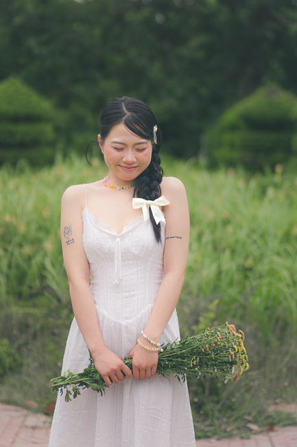 Smiling woman in a white dress holding wildflowers outdoors in a lush garden.