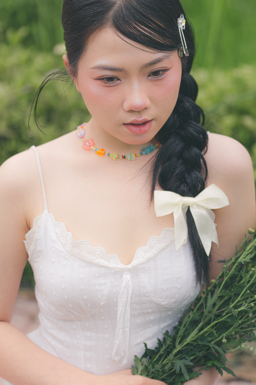 Free Young woman in a white dress with floral accessories, holding greenery in a serene outdoor setting. Stock Photo