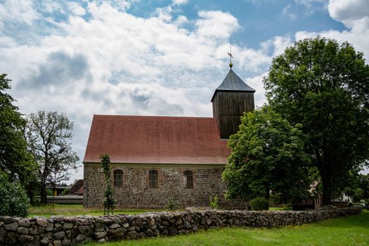 Charming rural church with brick architecture surrounded by lush greenery under a blue sky.