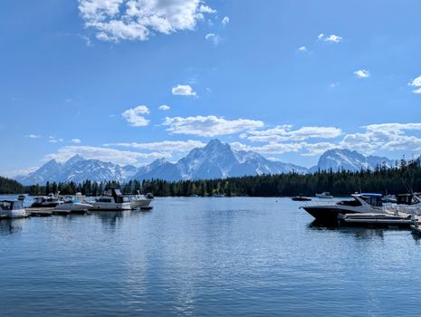 Tranquil marina scene with boats on a lake, framed by the majestic Grand Tetons under a clear blue sky.