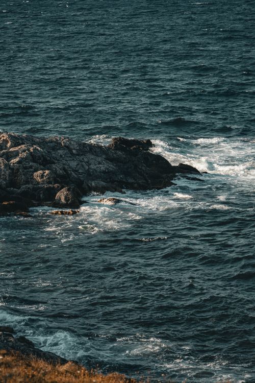 Free Waves crash against a rugged rocky shoreline under a moody sky, showcasing nature's raw power. Stock Photo