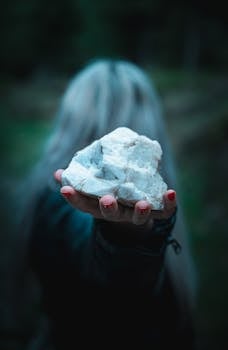 Close-up of a woman holding a large white stone with a blurred background, creating a mysterious vibe.
