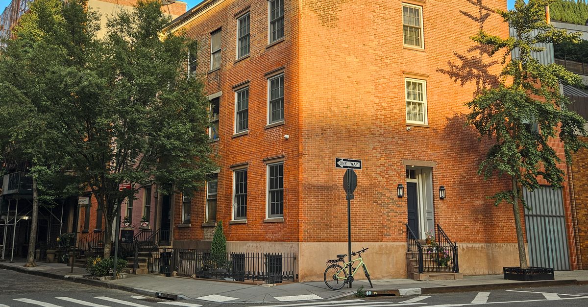 Sunlit brick building on a New York City street corner, showcasing classic architecture.