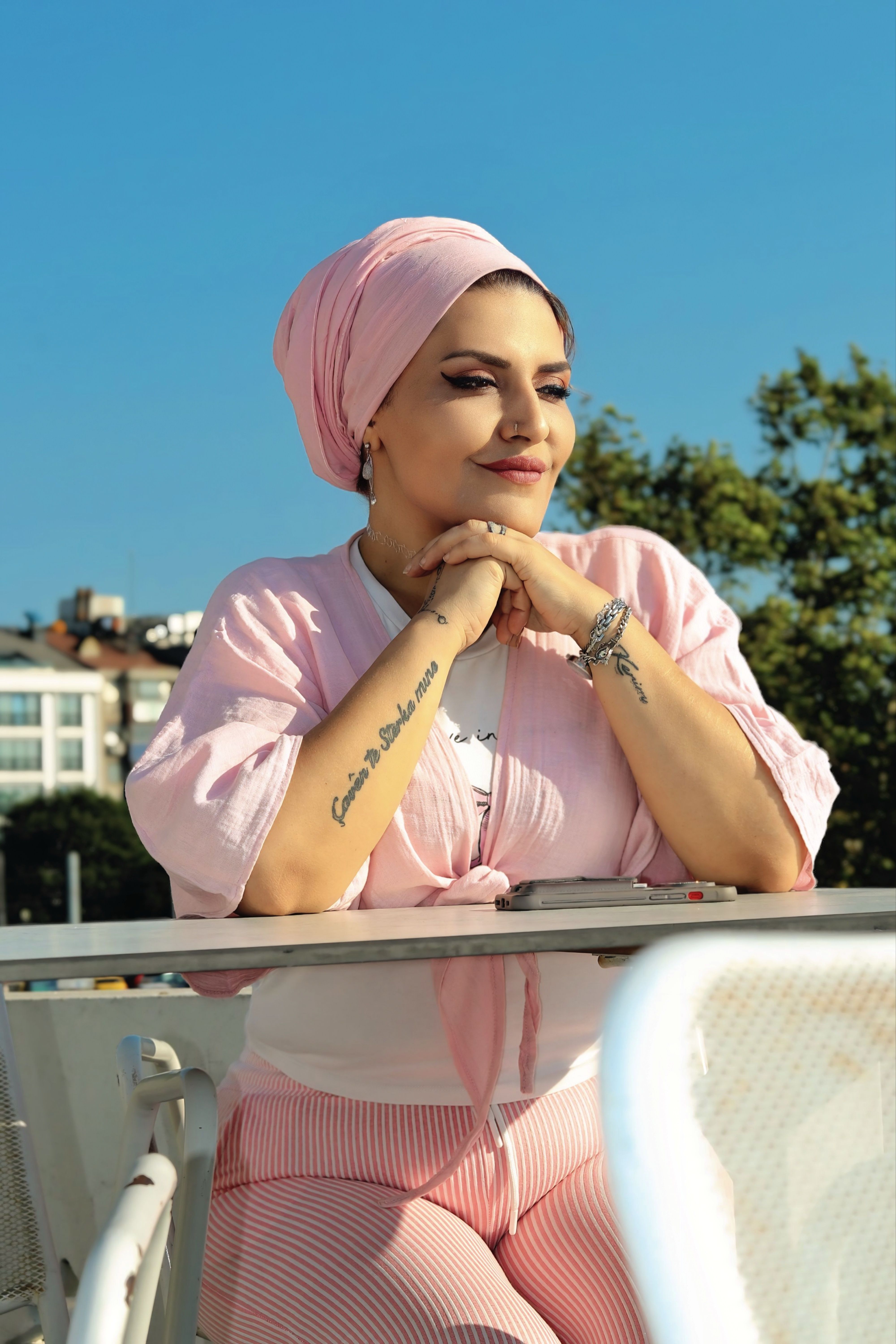 Elegant woman in pink attire enjoying a sunny day outdoors, looking content and relaxed.