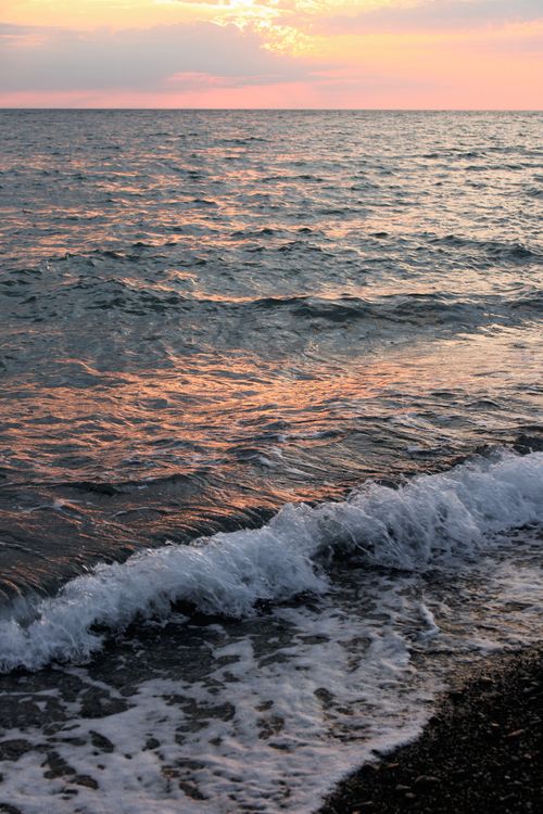 Free Capture the tranquil beauty of ocean waves at sunset with a serene glow on a pebble beach. Stock Photo