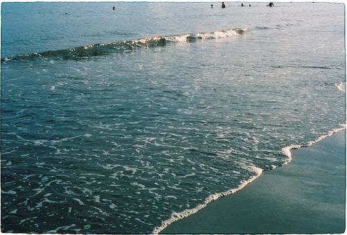 Free Tranquil beach scene with gentle waves and distant swimmers at sunset. Stock Photo