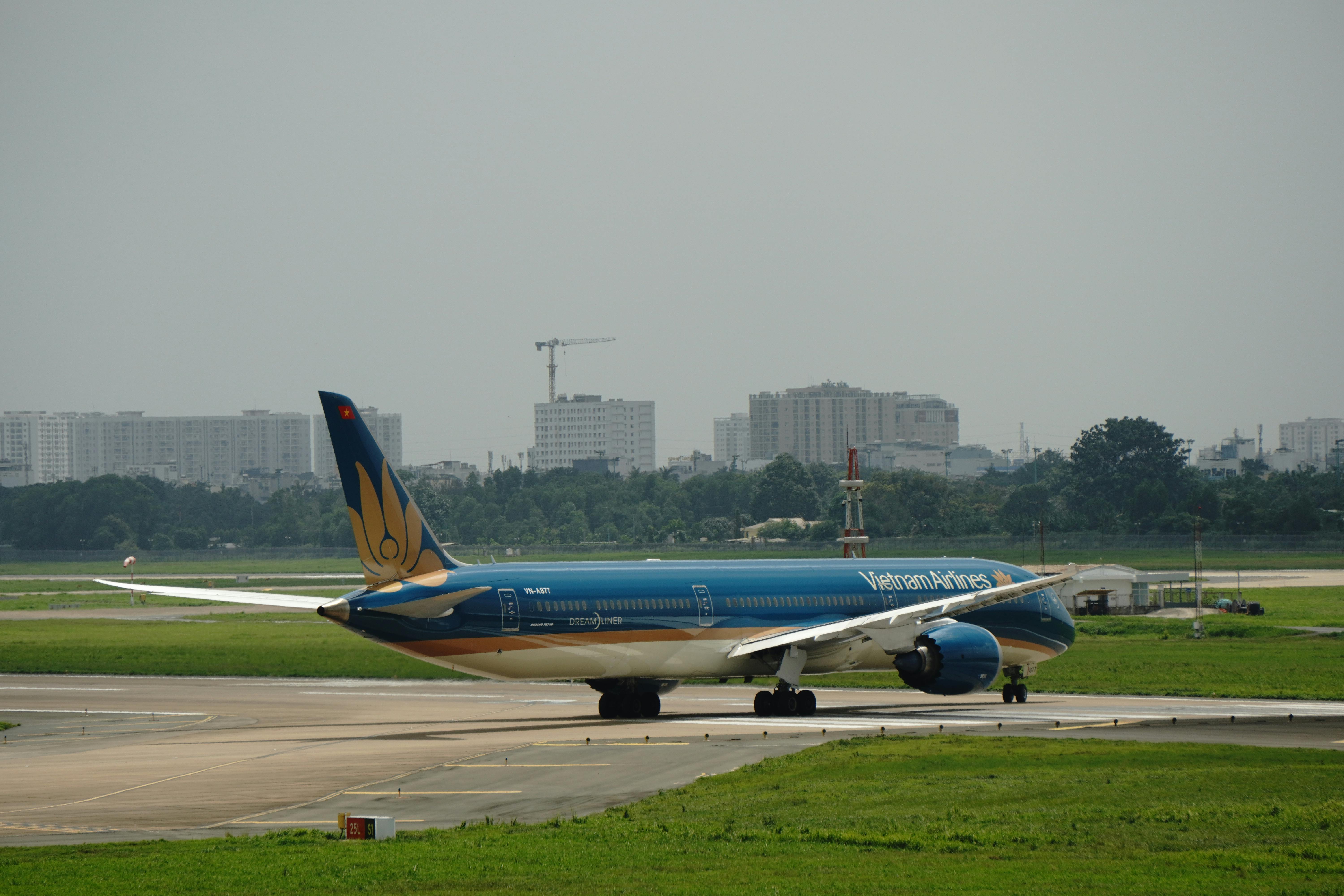 Eine Boeing 787 der Vietnam Airlines rollt auf einer Startbahn an einem Flughafen in Vietnam vor einer Stadtkulisse.